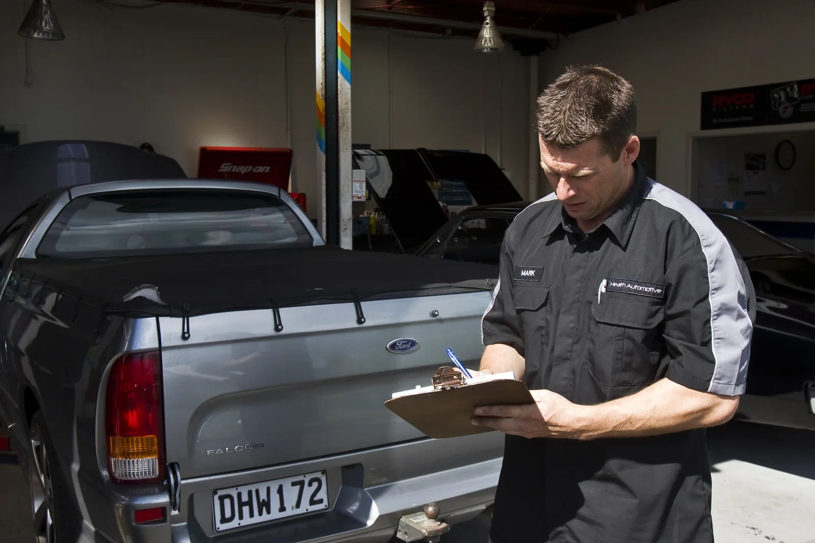 Technician with clipboard beside a Falcon ute